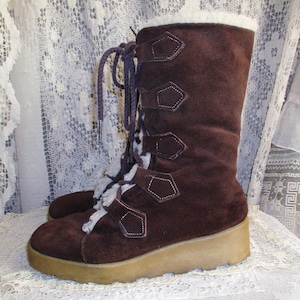 May include: A pair of brown suede boots with a cream-colored faux fur lining and a beige platform sole. The boots have decorative buckles and purple laces. The boots are a vintage style.