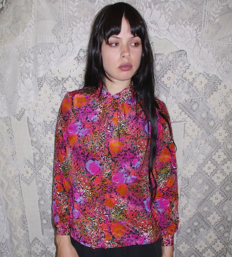 80s blouse with pleats in front and a pattern of bright floral and scribble pattern of  orange, pink, purple, green, white, and mustard yellow