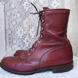 May include: A pair of burgundy leather boots. The boots have a lace-up design with metal eyelets and a short fringe detail on the toe. The boots have a sturdy sole and a mid-calf height.