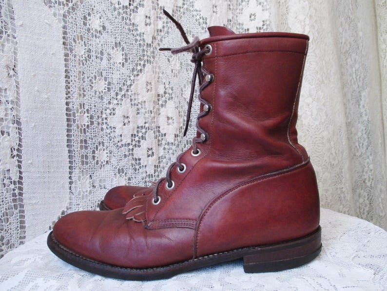 May include: A pair of burgundy leather boots. The boots have a lace-up design with metal eyelets and a short fringe detail on the toe. The boots have a sturdy sole and a mid-calf height.