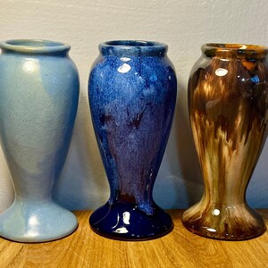 May include: Three ceramic vases with different glaze patterns. The vase on the left is light blue, the middle vase is blue and purple, and the vase on the right is brown and white.