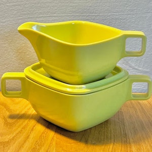 May include: A set of two yellow ceramic bowls with handles. The smaller bowl is stacked on top of the larger bowl.