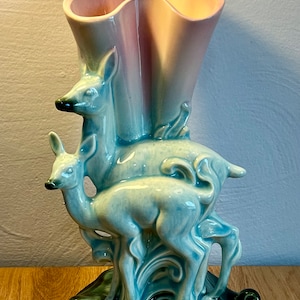 May include: A vintage ceramic vase with a pink and white glaze, featuring two stylized deer in a blue glaze, standing on a green base.