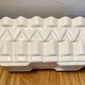 May include: White ceramic planter with a geometric design. The planter has a scalloped edge and a rectangular shape.