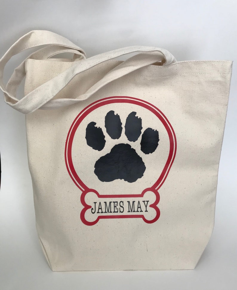 May include: A white canvas tote bag with red and black paw print design. The bag has red and black bone-shaped design with the text "JAMES MAY" inside.