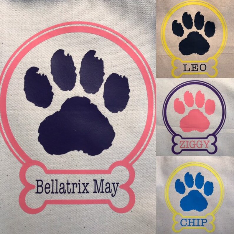 May include: Three personalized tote bags with paw print designs. The bags are white canvas with pink, purple, and yellow accents. The names on the bags are Bellatrix May, Ziggy, and Chip.