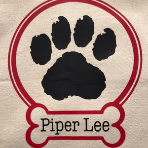 May include: A red bone-shaped design with the name "Piper Lee" printed in black text. A black paw print is inside a red circle.