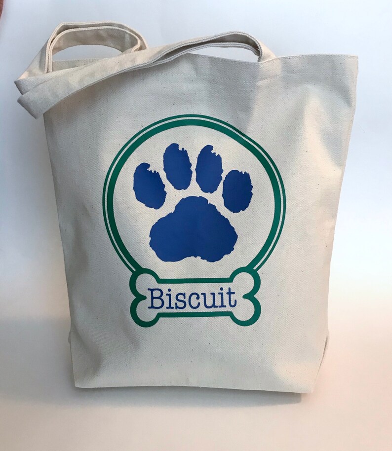 May include: A white canvas tote bag with a green circle and a blue paw print. The text "Biscuit" is written in a green bone shape.