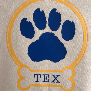 May include: A yellow bone-shaped design with the name "TEX" inside. A blue paw print is inside a double yellow circle.