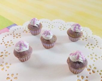 May include: Five miniature purple and white cupcakes with white frosting on a white doily.