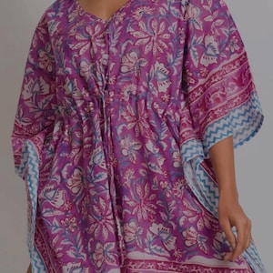 May include: A purple floral print kaftan with a V-neckline and drawstring waist. The kaftan features a repeating pattern of white and blue flowers on a purple background. The sleeves and hem are trimmed with a blue and white zigzag pattern.