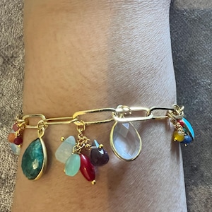 May include: A gold charm bracelet featuring a selection of colourful gemstone charms, including turquoise, emerald, red, and clear quartz.