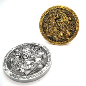 Puede incluir: Dos monedas redondas de metal con un diseño detallado de dos peces nadando en direcciones opuestas. Las monedas son de color dorado y plateado y presentan el texto "Dum Spiro Spero" en una pancarta.