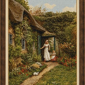 May include: A framed cross-stitch embroidery depicting a cottage with a thatched roof, a lush garden, and two figures standing in an open doorway. A small white animal sits on a dirt path leading toward the house, surrounded by green foliage.