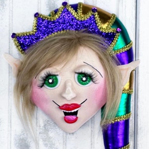 May include: A whimsical elf doll head with blonde hair, green eyes, and a bright red smile. The elf is wearing a purple and gold crown and a green and purple jester hat.