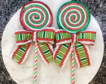 May include: Two red and green swirl lollipop ornaments with white polka dots and green and red striped bows. The lollipops are attached to red and white striped sticks.