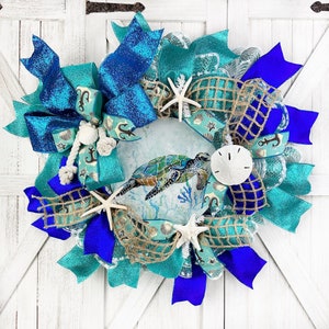 May include: A teal, blue, and white wreath with a sea turtle design, blue and teal ribbon, burlap, and seashells.