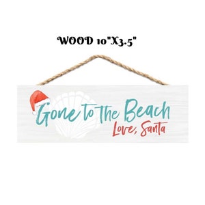 Może przedstawiać: Drewniany znak o wymiarach 25,4 cm x 8,9 cm, z wieszakiem ze sznurka. Znak głosi "Gone to the Beach Love, Santa" w turkusowych i czerwonych literach, z czapką Świętego Mikołaja i muszlą.