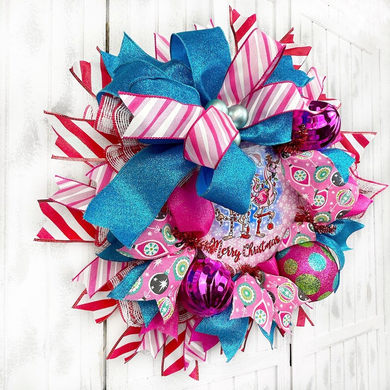 K&ouml;nnte beinhalten: Ein Weihnachtskranz in den Farben Pink, Blau und Wei&szlig;. Der Kranz hat ein festliches Design mit Ornamenten, B&auml;ndern und einem Schild mit der Aufschrift "Frohe Weihnachten".