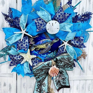 May include: A blue and white wreath with a sea turtle, starfish, and seashells. The wreath is decorated with blue and white ribbon and a burlap bow.