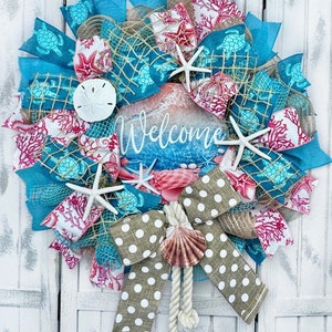 May include: A teal, white, and red summer wreath with a burlap bow, seashells, starfish, and a sign that says "Welcome".