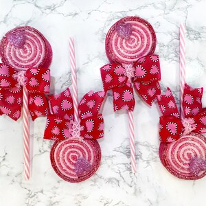 May include: Four pink and white swirl lollipop decorations with pink and white heart patterned bows attached to each lollipop.