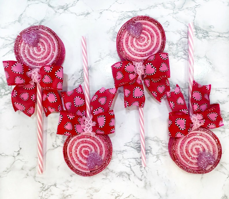 May include: Four pink and white swirl lollipop decorations with pink and white heart patterned bows attached to each lollipop.
