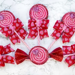 May include: Six pink and red glitter swirl lollipops with white sticks and red and pink heart patterned bows.