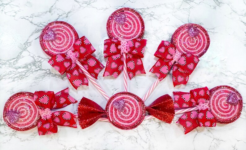 May include: Six pink and red glitter swirl lollipops with white sticks and red and pink heart patterned bows.