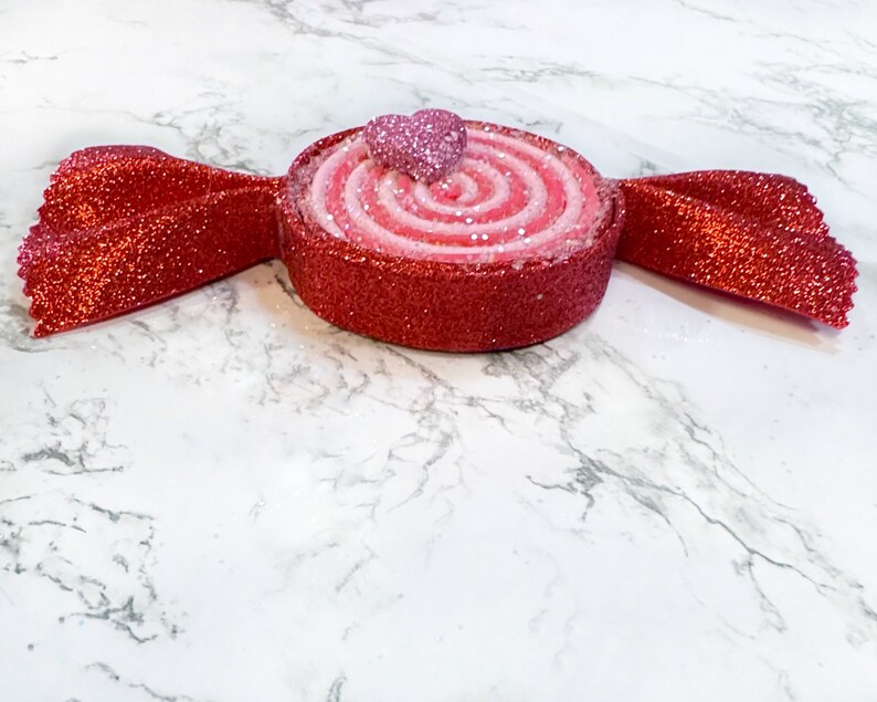 May include: A red and pink candy cane shaped ornament with a glitter finish. The candy cane is topped with a pink heart.
