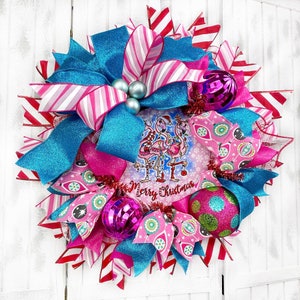 K&ouml;nnte beinhalten: Ein rosa-blauer Weihnachtskranz mit einem Flamingo-Motiv und dem Text "Merry Christmas". Der Kranz ist mit rosa-blauen Schleifen, Glitzer und Kugeln verziert.