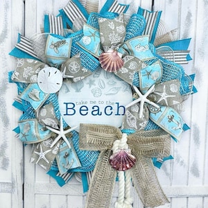 May include: A turquoise and beige wreath with a sign that reads "Take me to the Beach". The wreath is decorated with seashells, starfish, and nautical-themed ribbons.
