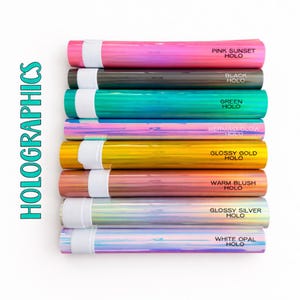 A collection of colorful, metallic-looking tubes or tubes with various colors and labels, such as "PINK SUNSET HOLO", "BLACK HOLO", "GREEN HOLO", "MERMAID GLOW HOLO", "GLOSSY GOLD HOLO", "WARM BLUSH HOLO", and "WHITE OAL HOLO".