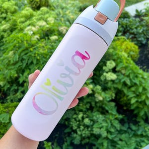 A person's hand holding a white water bottle with the name "Olivia" printed on it.