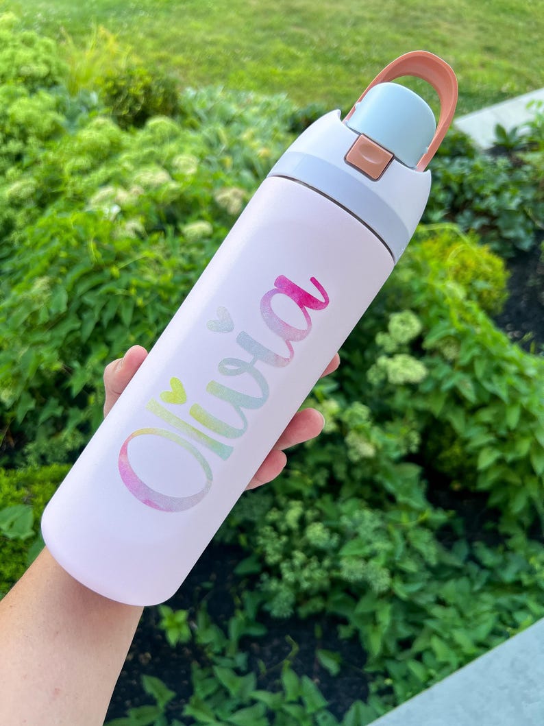 A person's hand holding a white water bottle with the name "Olivia" printed on it.
