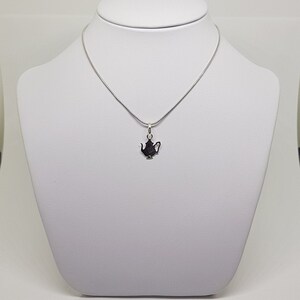 May include: A silver chain necklace with a silver teapot pendant. The teapot is a simple silhouette.