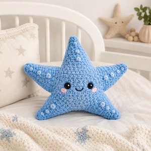 May include: A light blue crochet starfish plush toy with five points, featuring small raised circular textures, black safety eyes, a stitched black smile, and two small pink embroidered circles on the cheeks to represent a blushing expression.