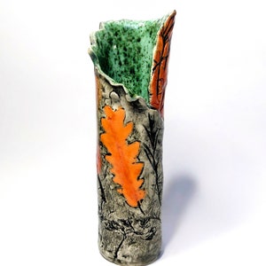 May include: A ceramic vase with a textured, grey and black exterior. The vase has a green and orange glaze with a leaf design.