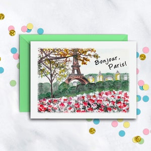 May include: A watercolor painting of the Eiffel Tower in Paris, France. The tower is surrounded by trees and flowers. The text "Bonjour, Paris!" is written in black ink on the card.