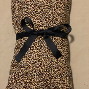 May include: A rectangular item wrapped in fabric with a leopard print pattern in shades of brown and tan. A black ribbon is tied around the center in a bow. The item appears to be a pillow or a similar soft product.