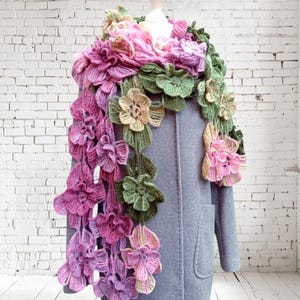 May include: A crocheted scarf with pink, green, and beige flowers. The scarf is draped over a gray coat.
