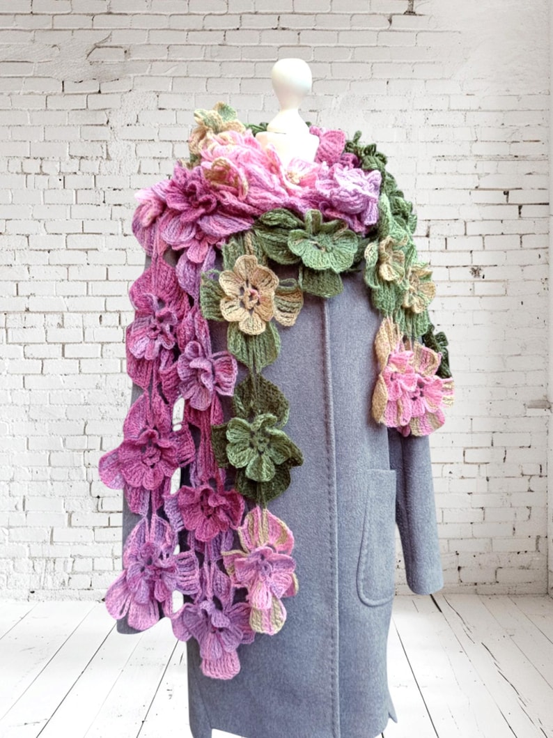 May include: A crocheted scarf with pink, green, and beige flowers. The scarf is draped over a gray coat.