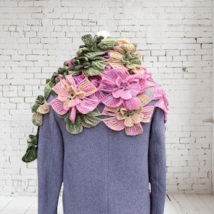 May include: A gray coat with a crocheted floral shawl in shades of pink, green, and beige. The shawl is made of delicate flowers and leaves.