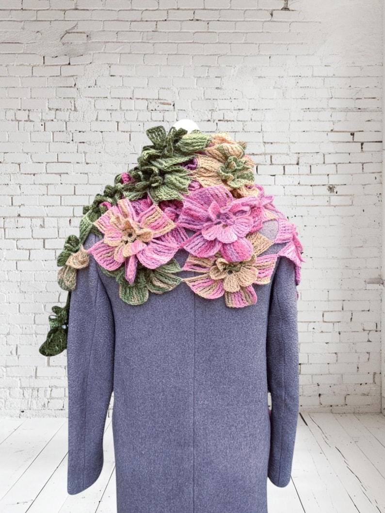 May include: A gray coat with a crocheted floral shawl in shades of pink, green, and beige. The shawl is made of delicate flowers and leaves.