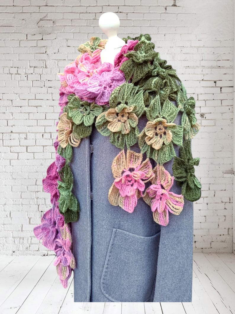 May include: A crocheted scarf with pink, green, and beige flowers. The scarf is draped over a gray coat.