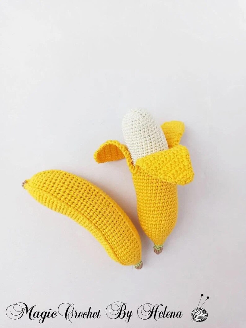 Puede incluir: Dos juguetes de pl&aacute;tano tejidos a crochet. Un pl&aacute;tano est&aacute; entero y el otro est&aacute; partido para revelar un interior tejido a crochet blanco.