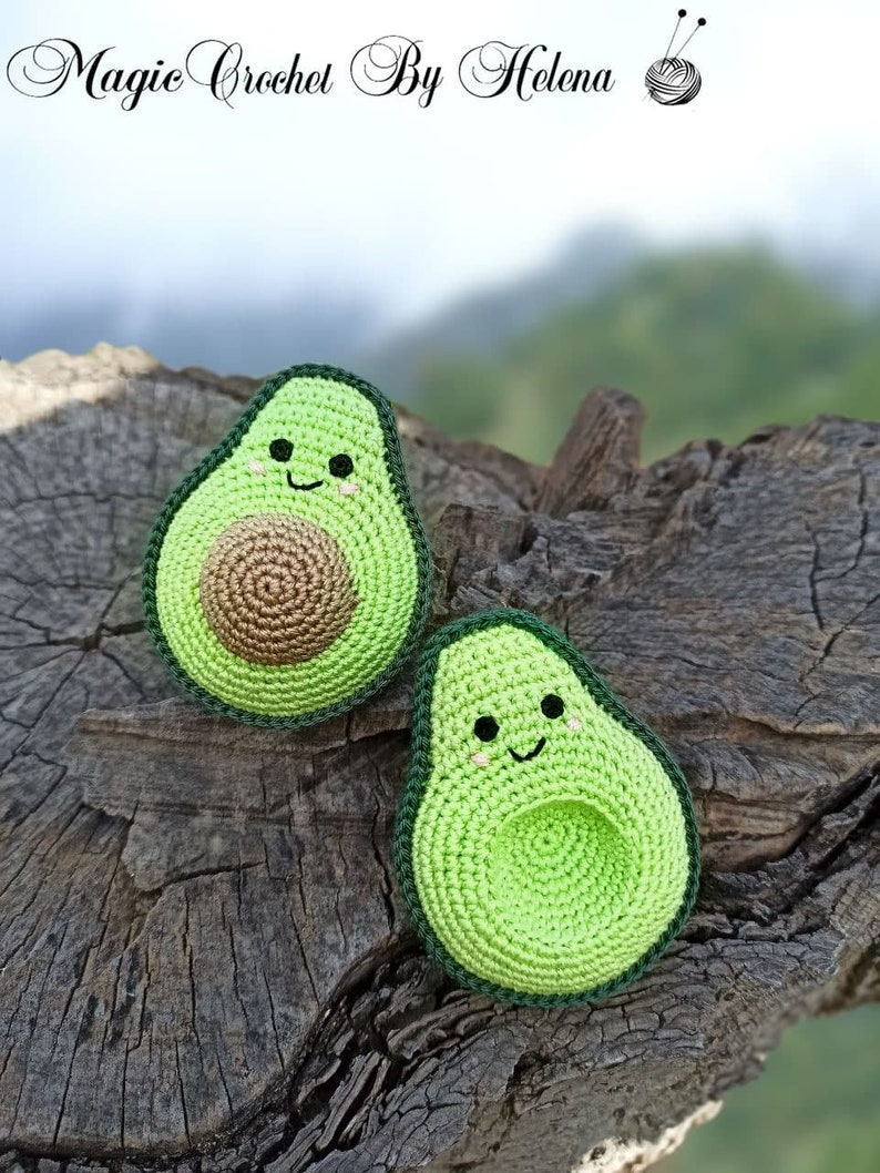 May include: Two crocheted avocado plushies with smiling faces. The avocados are green with brown pits and are sitting on a wooden surface.