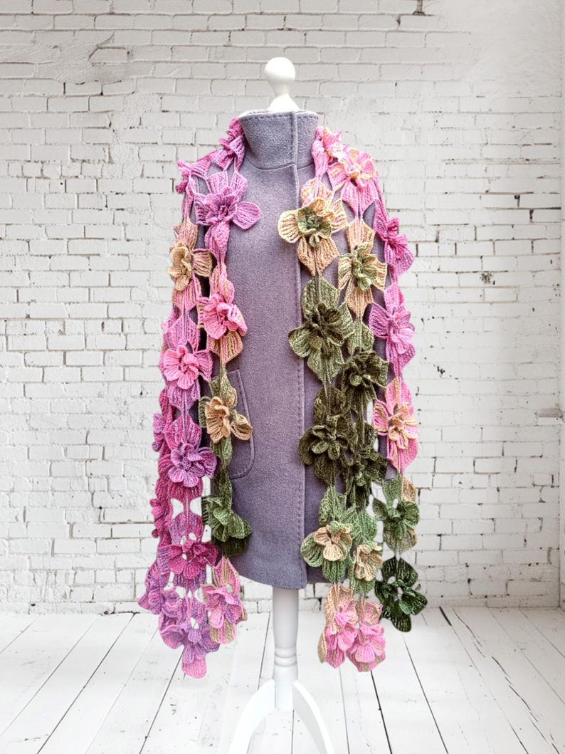 May include: A crocheted scarf with pink, green, and yellow flowers. The scarf is draped over a white mannequin.