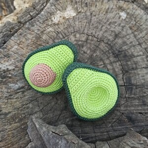 May include: Two crocheted avocado halves, one with a brown pit and the other with a green pit, on a wooden surface.