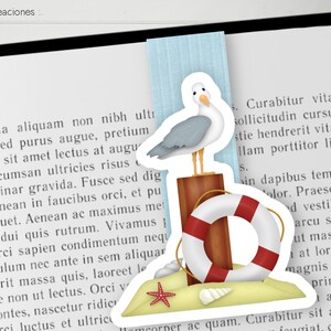 Può includere: Un adesivo con un gabbiano dei cartoni animati appollaiato su un palo di legno con un salvagente rosso e bianco. L'adesivo è su uno sfondo di sabbia, una conchiglia e una stella marina rossa.